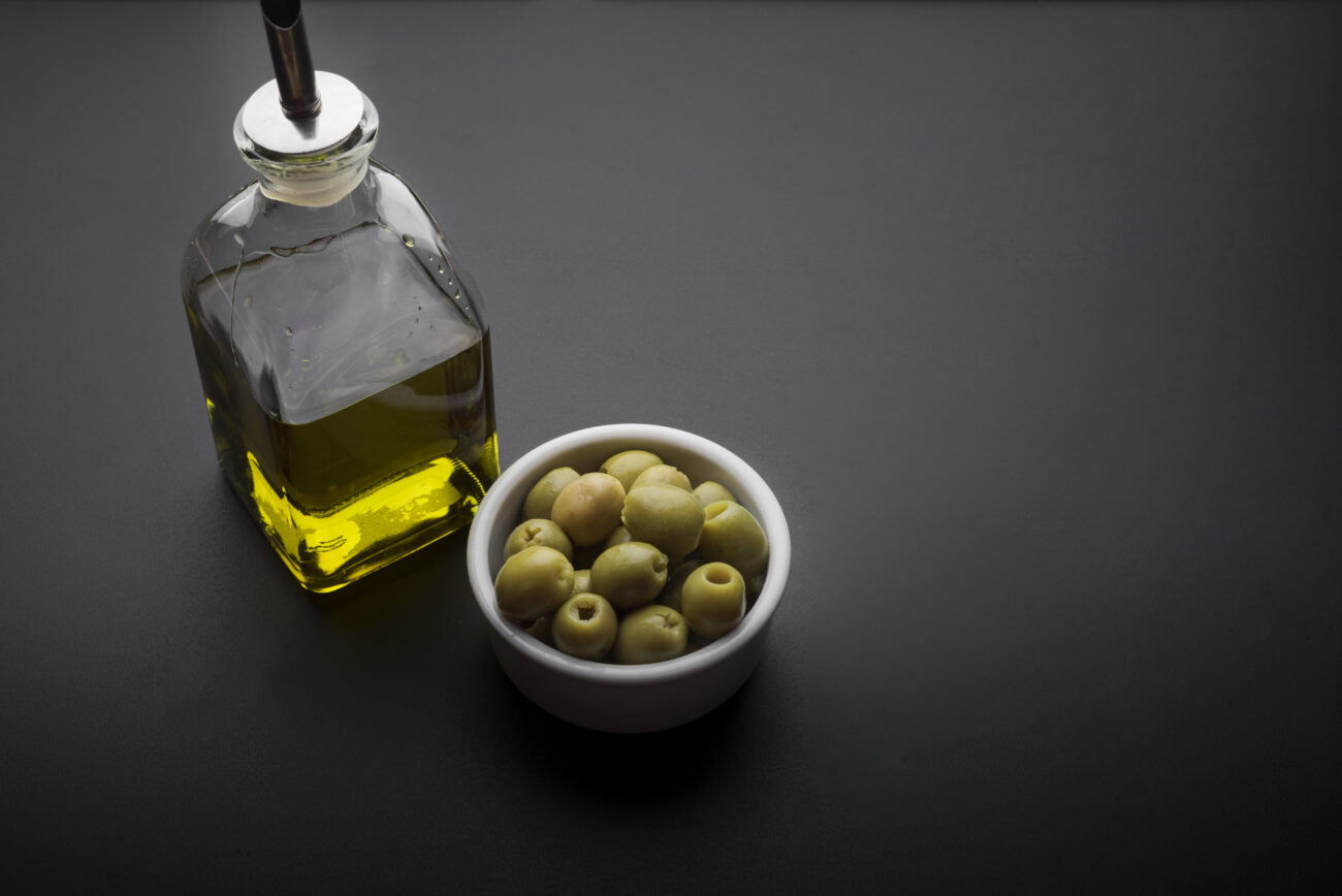 alt="Extra virgin olive oil for skin with fresh olives and leaves - benefits, how to use on face and natural skincare"